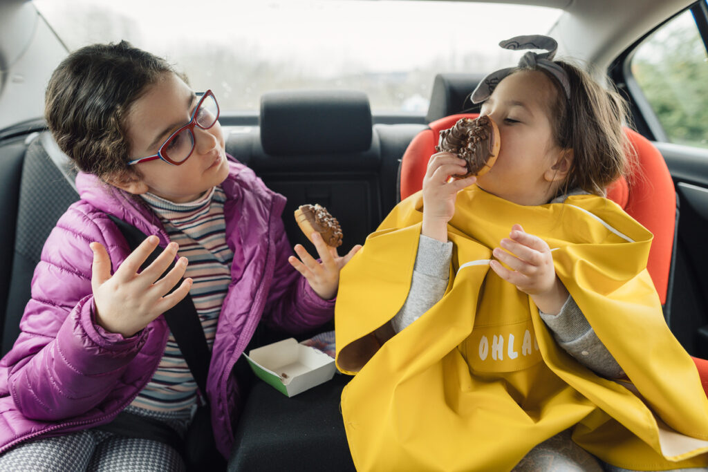 Two sisters eating in the back seat of a car